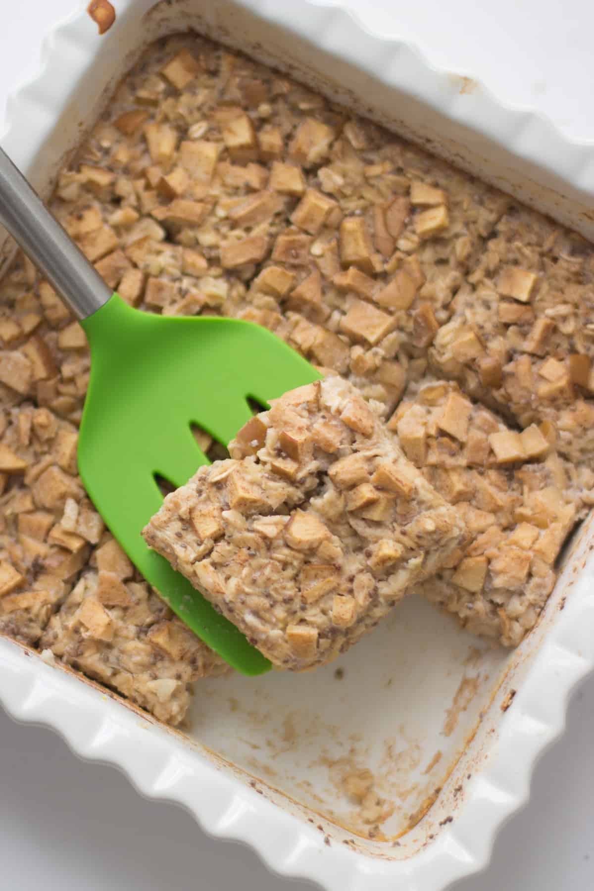 An overhead shot of baked oatmeal with slice on green spatula.