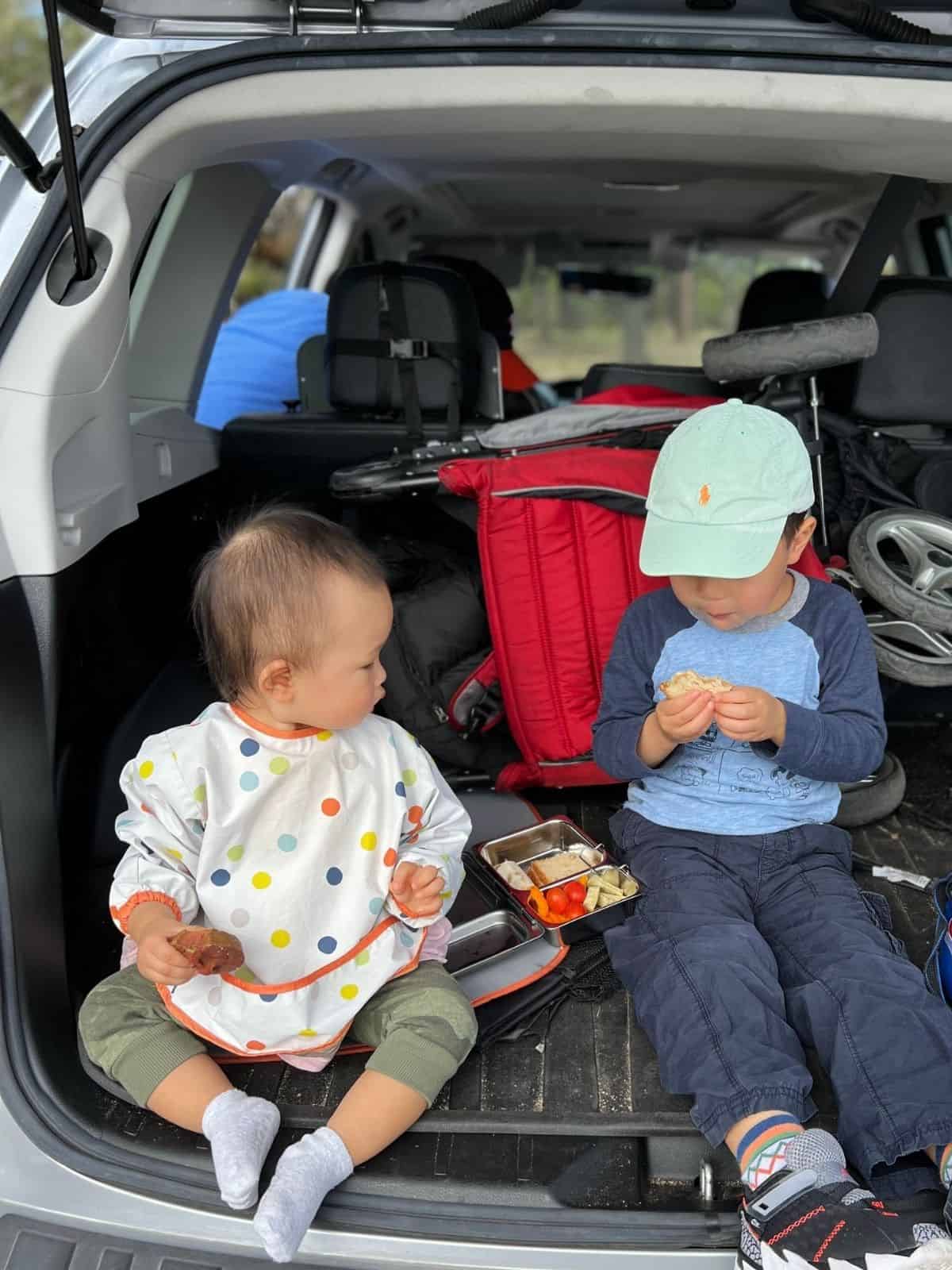 Two toddlers eating in the car trunk.