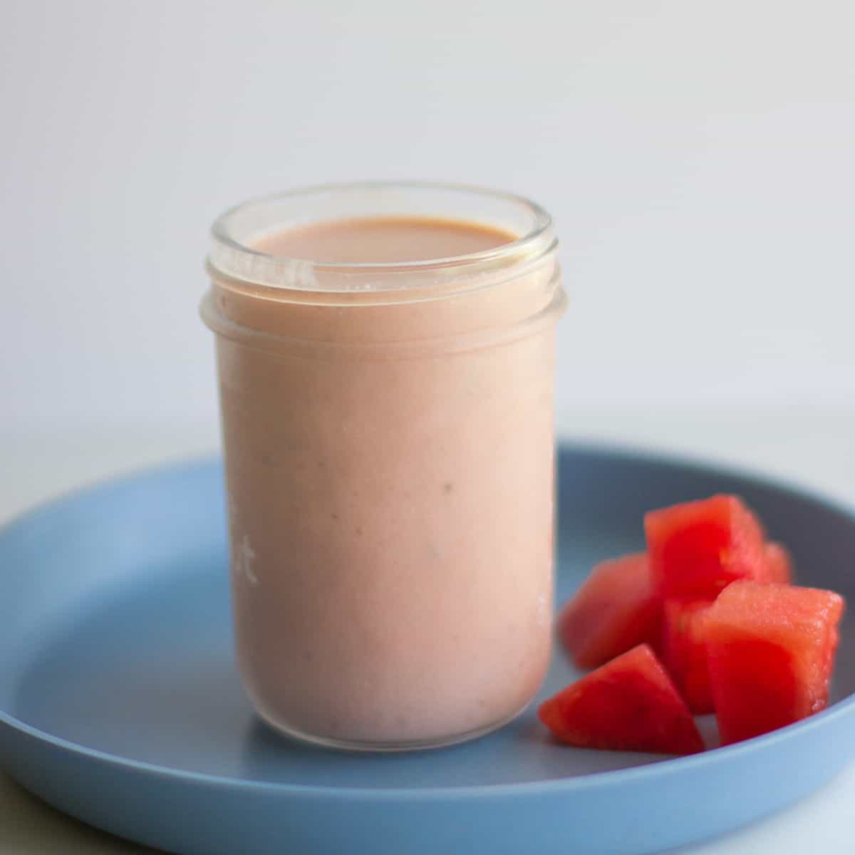 Smoothie in a glass jar with cubed watermelon on the side.