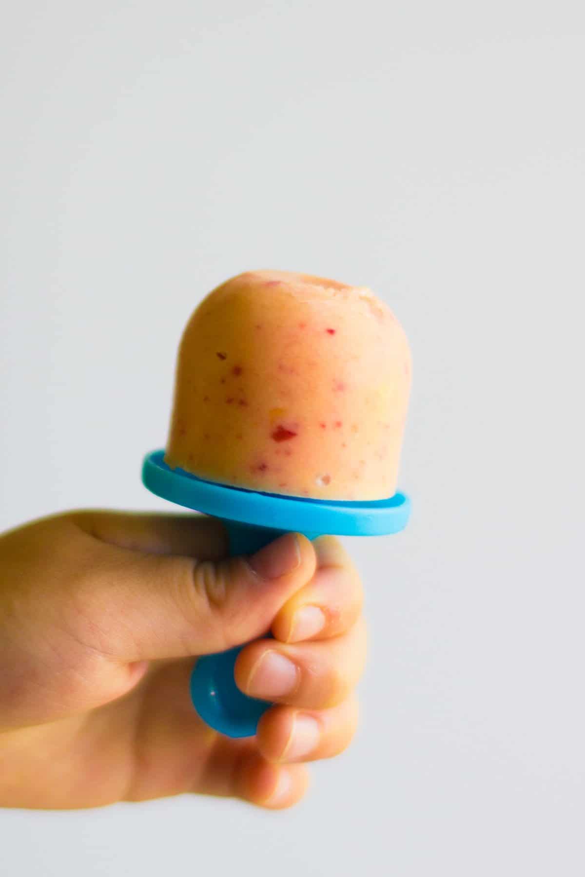 Toddler's hand holding a small peach yogurt popsicle.