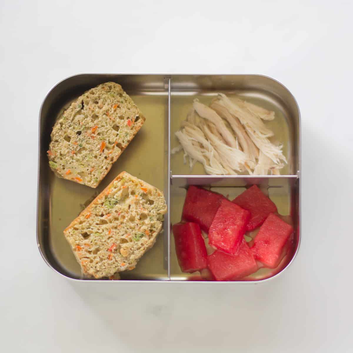 A sliced vegetable muffin in a school bento box with shredded chicken and watermelon.