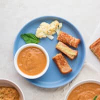 A small portion of tomato soup with sliced grilled cheese, cauliflower, and one basil.