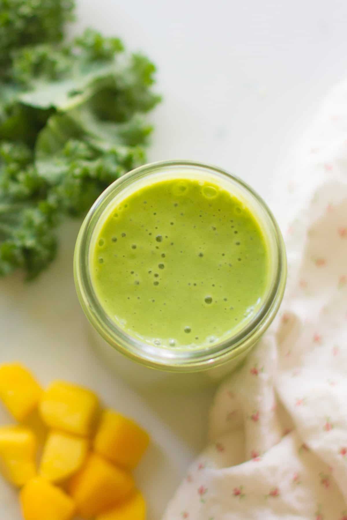 An overhead shot of smoothie with kale and mangoes in the background.