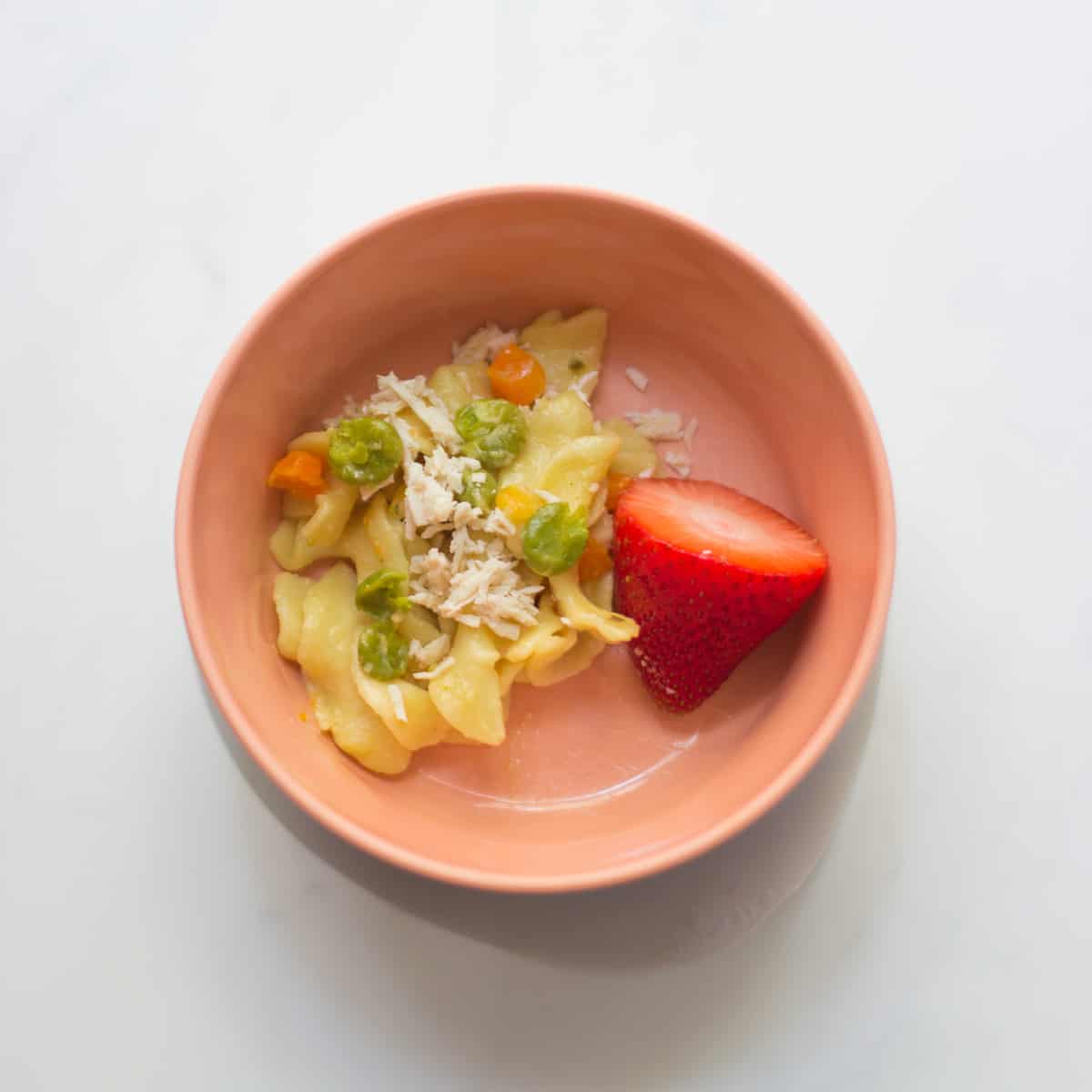 A small portion of IP chicken and noodles with a large strawberry in a baby bowl.