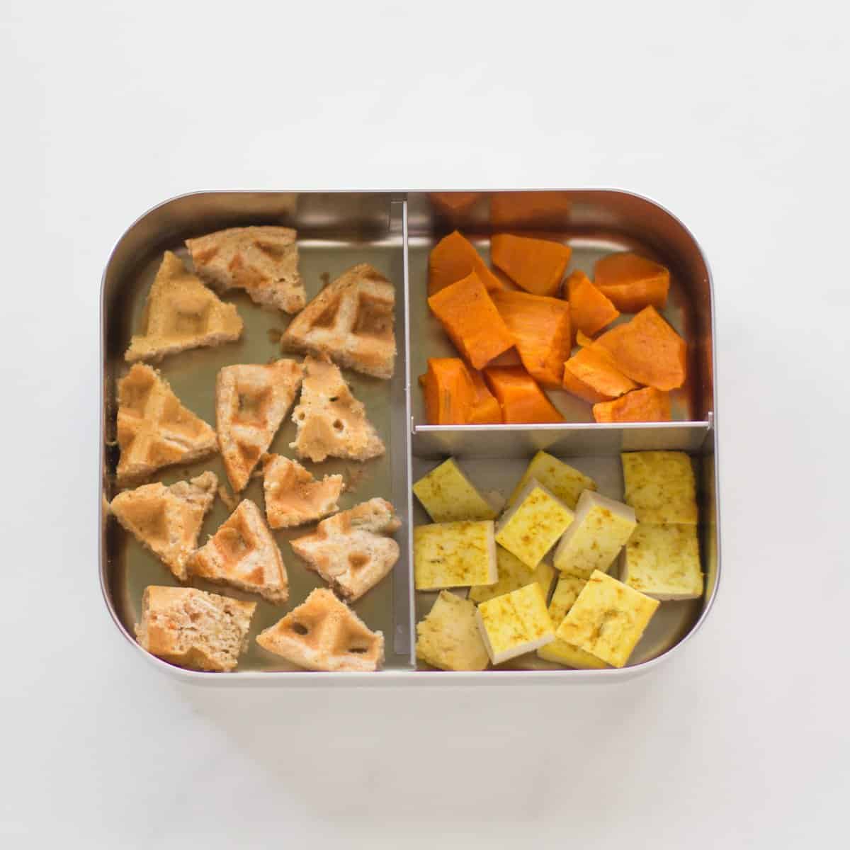 waffles, carrots, and tofu cut into bite-sized pieces in a stainless steel bento box.