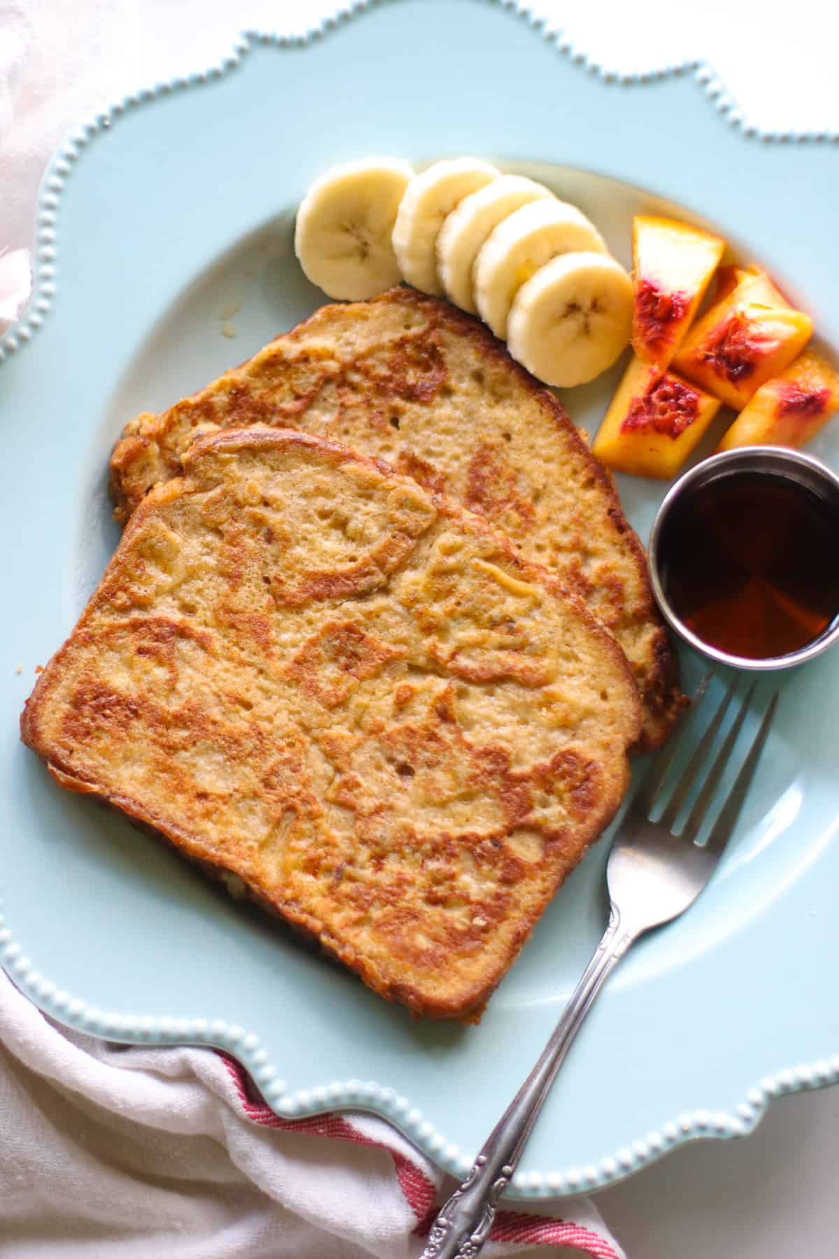 2 slices of French toast with banana, peaches, and syrup.