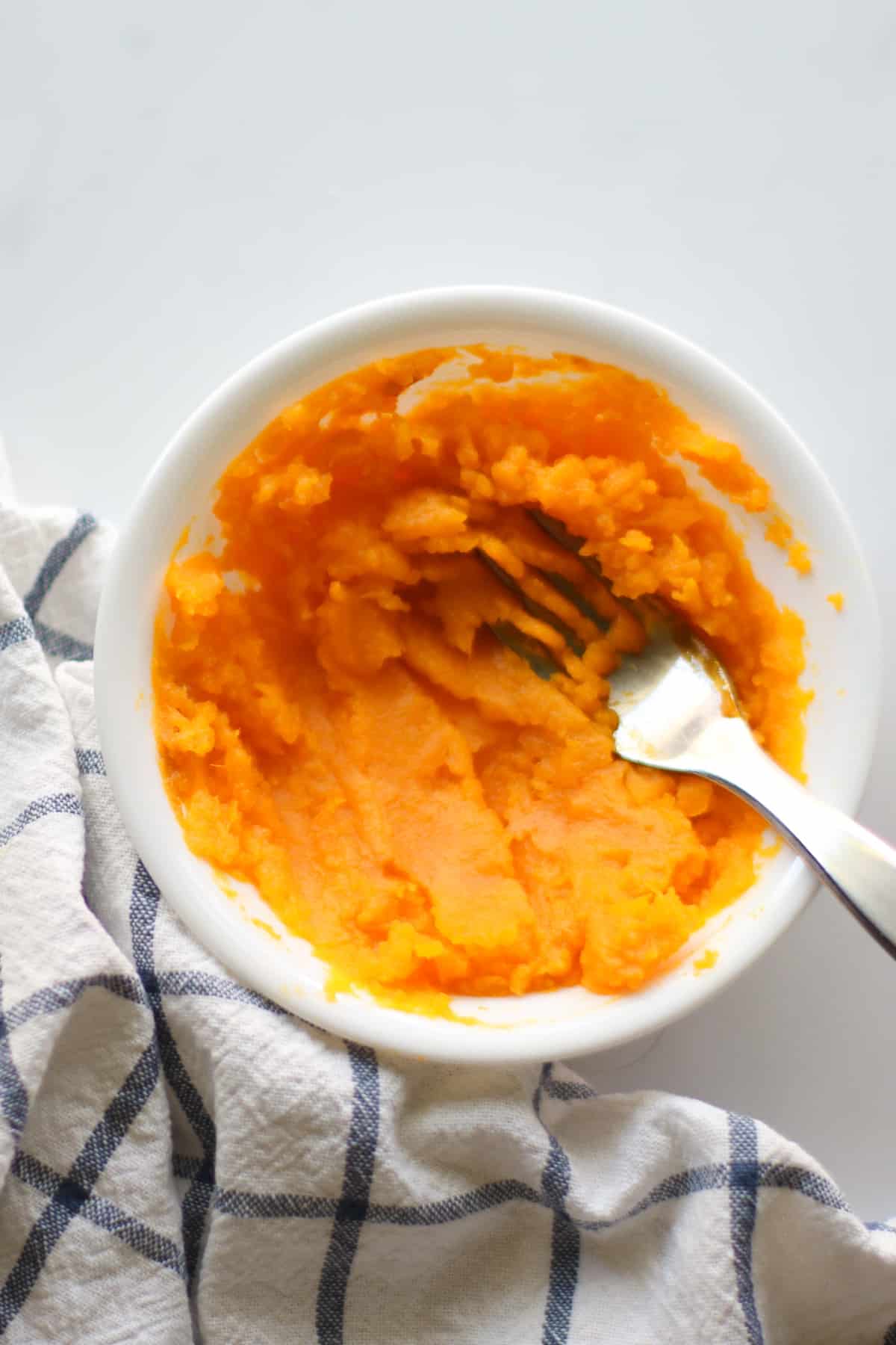 Mashed pumpkin in a white bowl with a fork.
