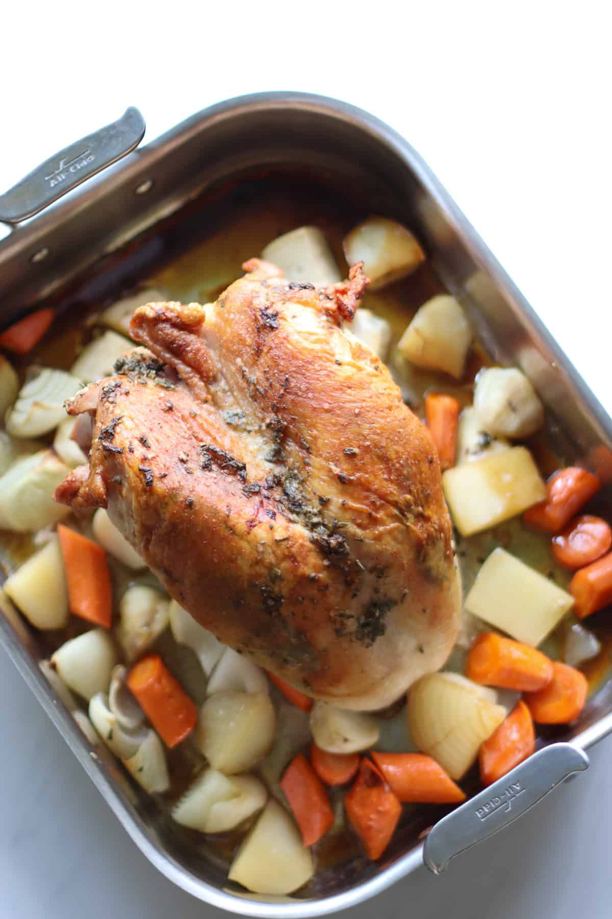 Roasted turkey breast on top of vegetables in a baking pan.