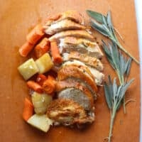 Sliced roasted turkey breast with vegetables and fresh sage.