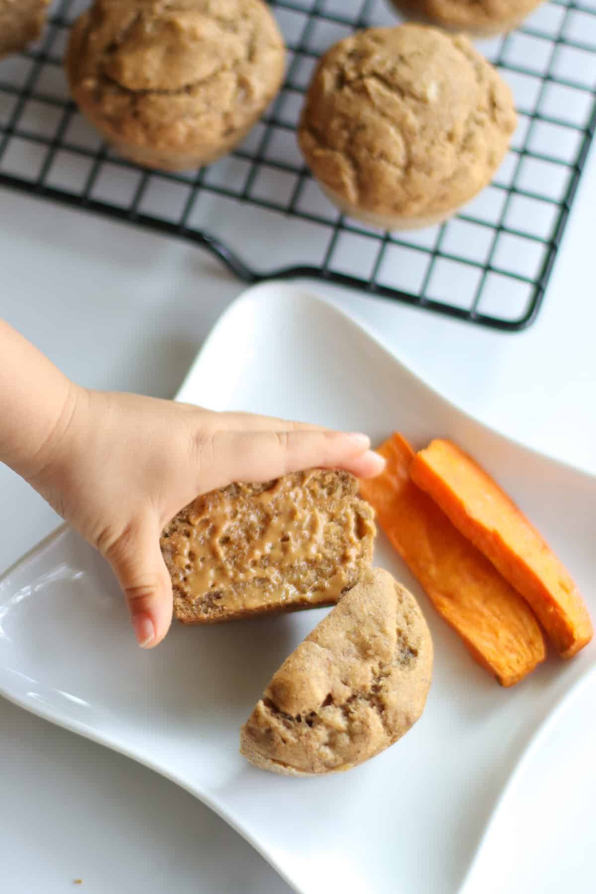 Toddler's hand reaching for halved muffin spread with peanut butter.