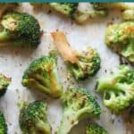 A close up shot of crispy roasted frozen broccoli on a lined baking sheet.