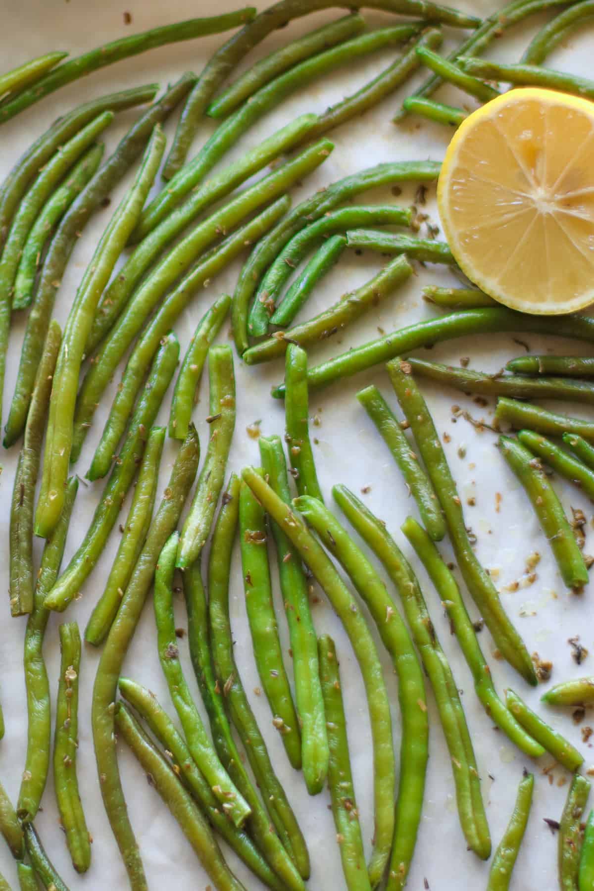 Roasted green beans on a baking sheet with a lemon slice.