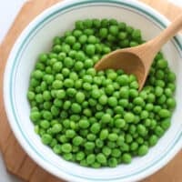Cooked frozen peas in a bowl with a wooden spoon.