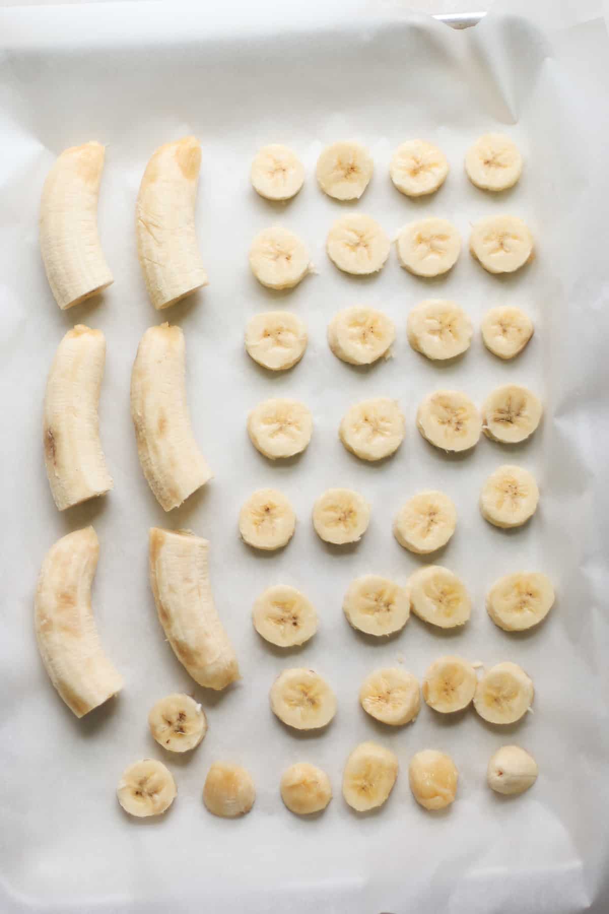 Sliced and halved bananas placed on a lined baking sheet.