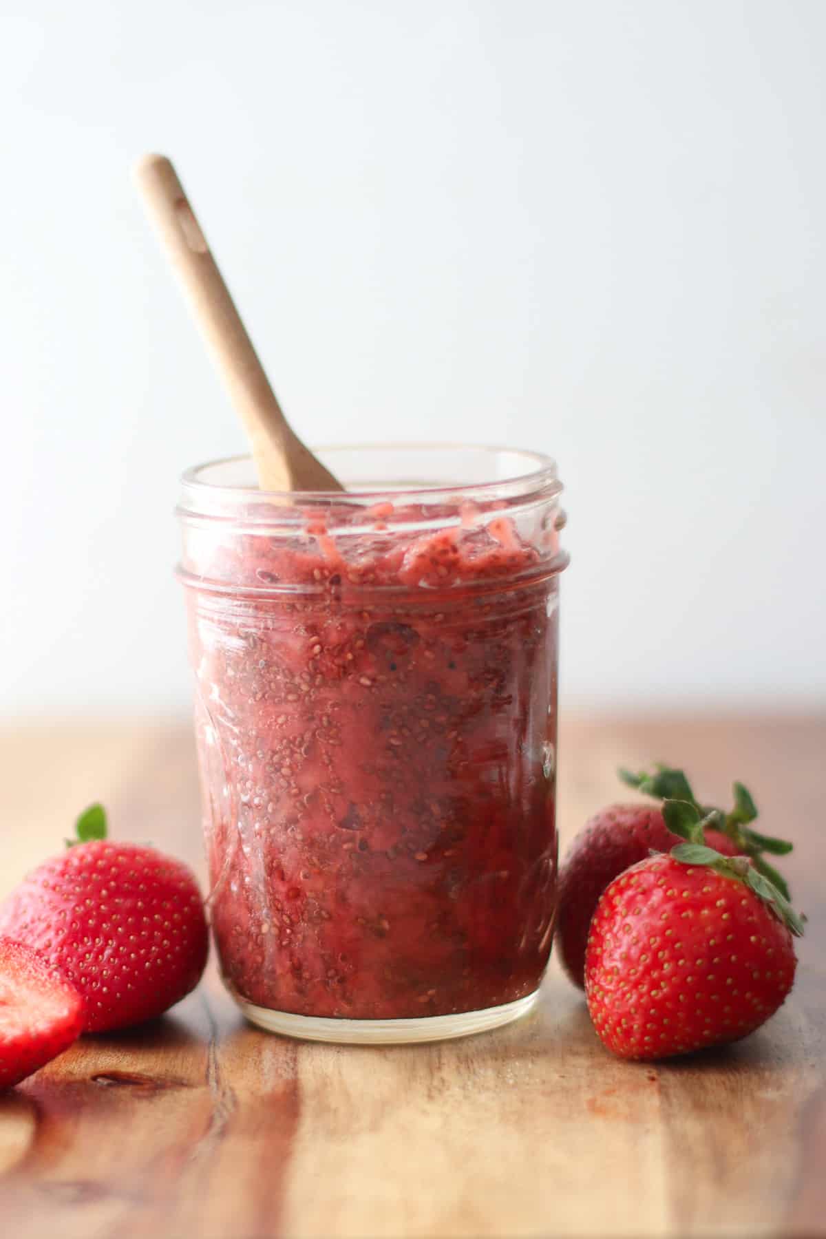 a side view of strawberry jam in a mason jar with a spoon.