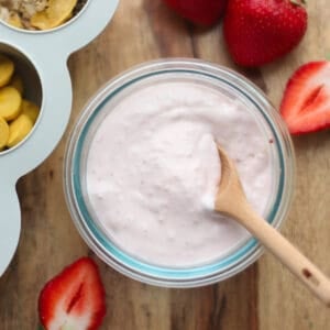 A close up shot of strawberry yogurt with strawberries in the backgrounnd.