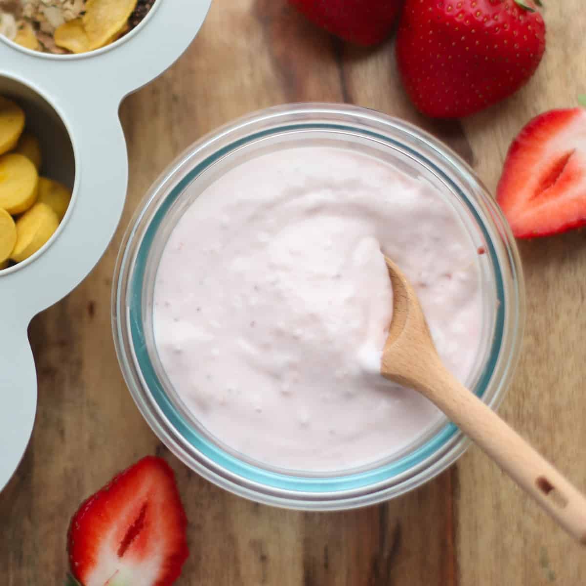 A close up shot of strawberry yogurt with strawberries in the backgrounnd.