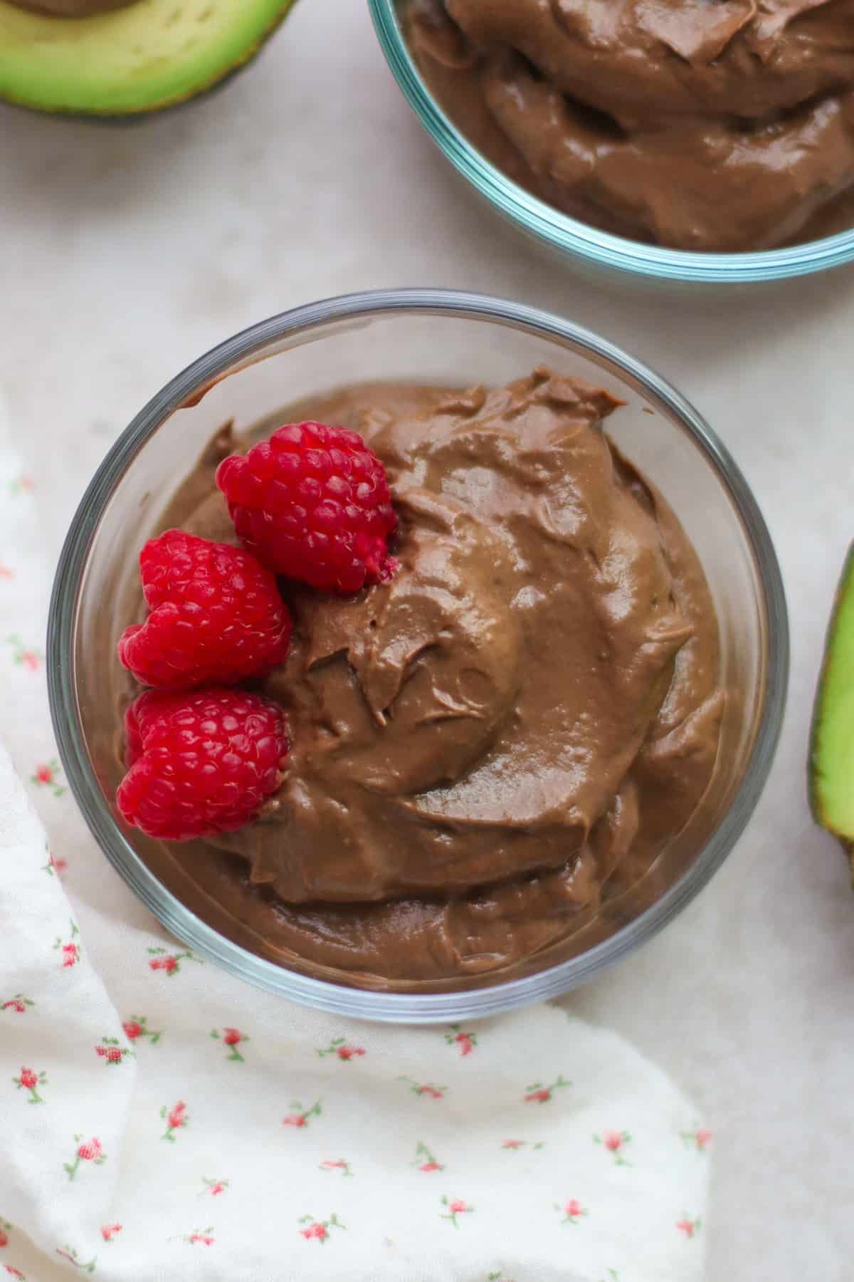 A close up overhead shot of chocolate pudding in a glass bowl with three raspberries.