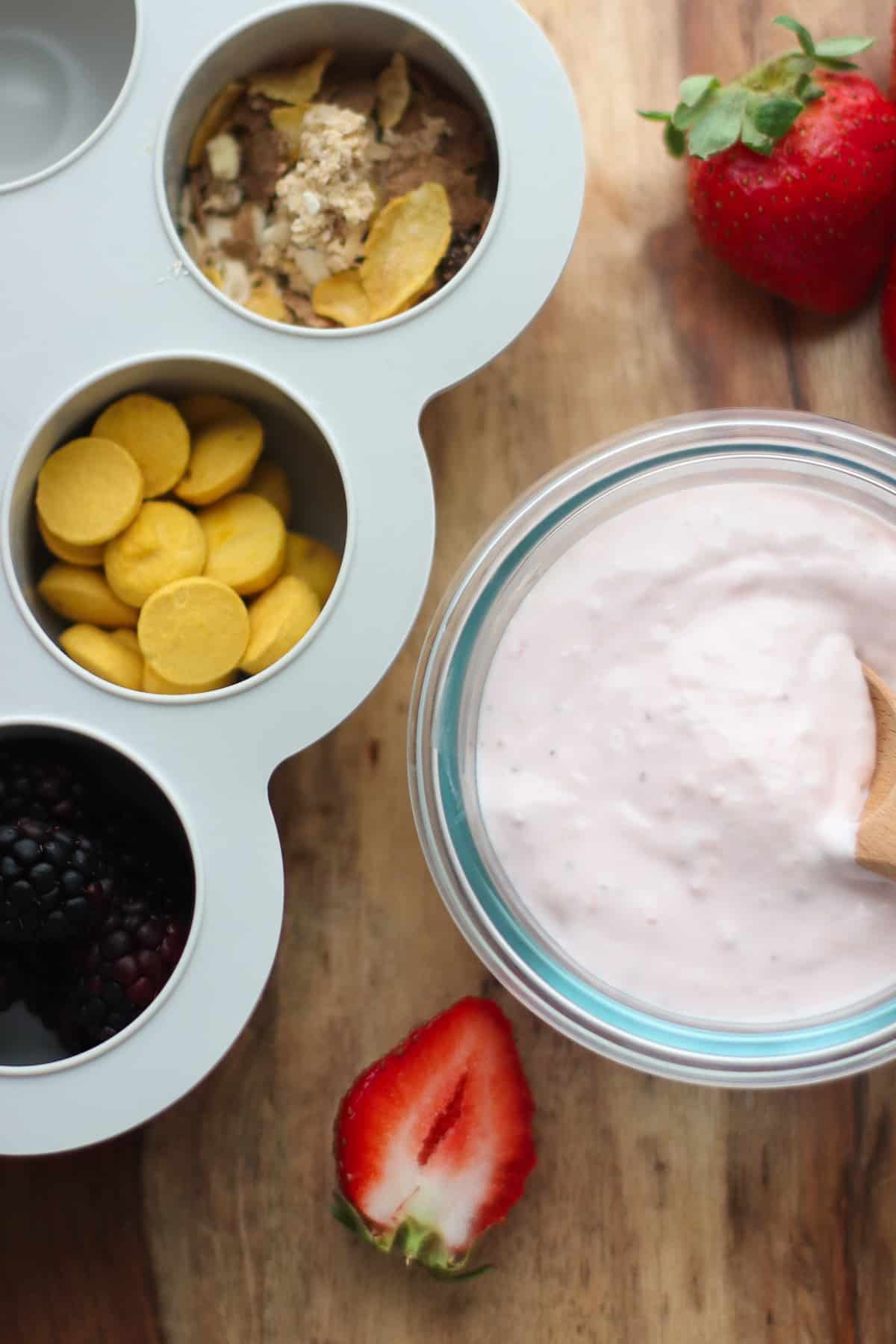 Yogurt melts, granola, and blackberries in muffin pan next to yogurt.