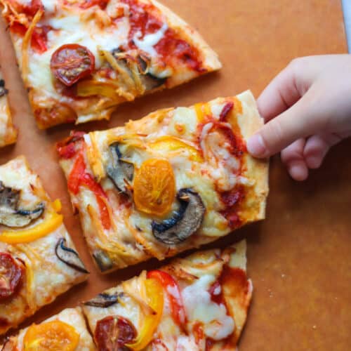 Sliced protein pizza with toddler's hand grabbing one.