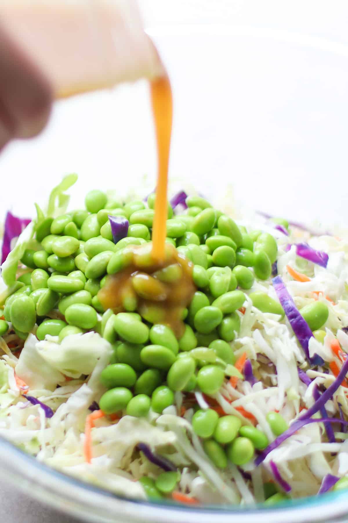 Dressing being poured over cabbage salad with edamame.