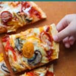 Sliced protein pizza with toddler's hand grabbing one.