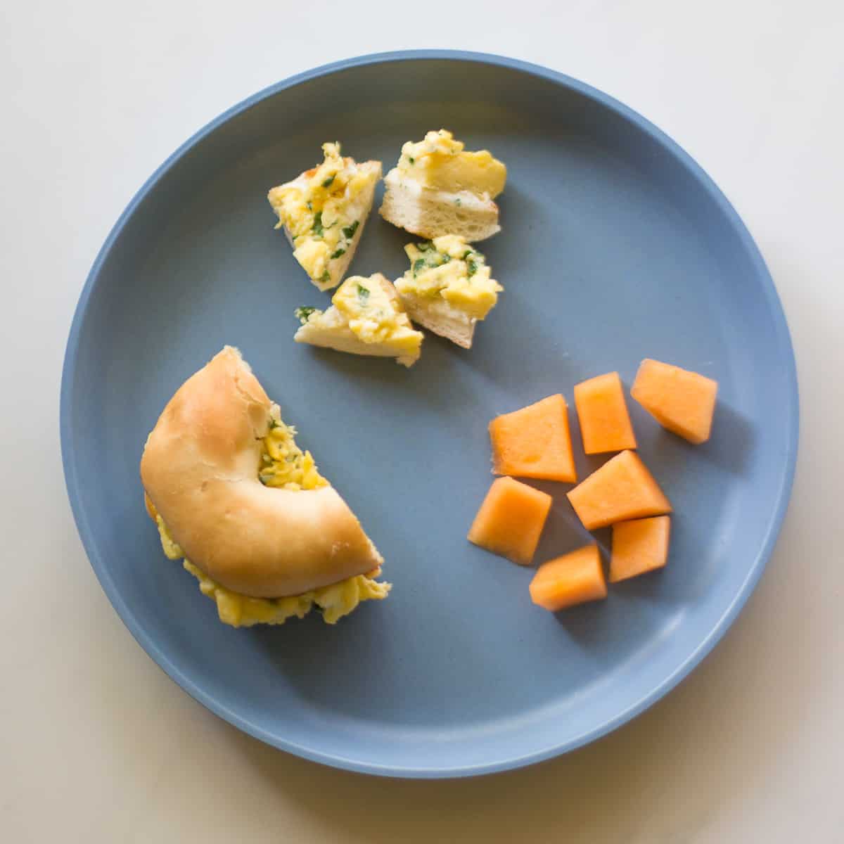 Halved egg salad bagel sandwich with bite-sized pieces and butternut squash.