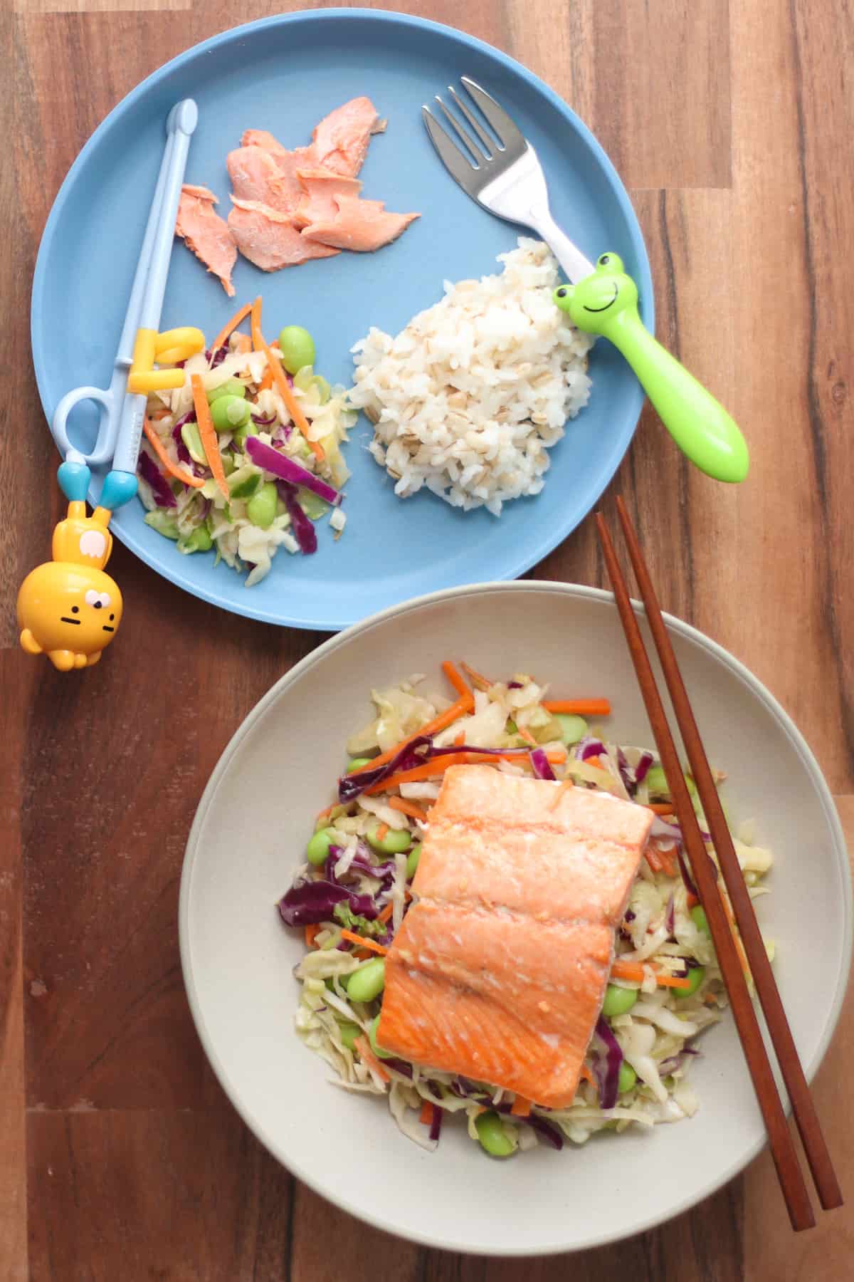 Cabbage salad with a whole salmon fillet for adult's plate and toddler's plate with rice, salad, and salmon pieces.