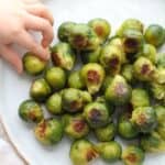 Roasted frozen brussels sprouts on a plate with a baby's hand grabbing one.