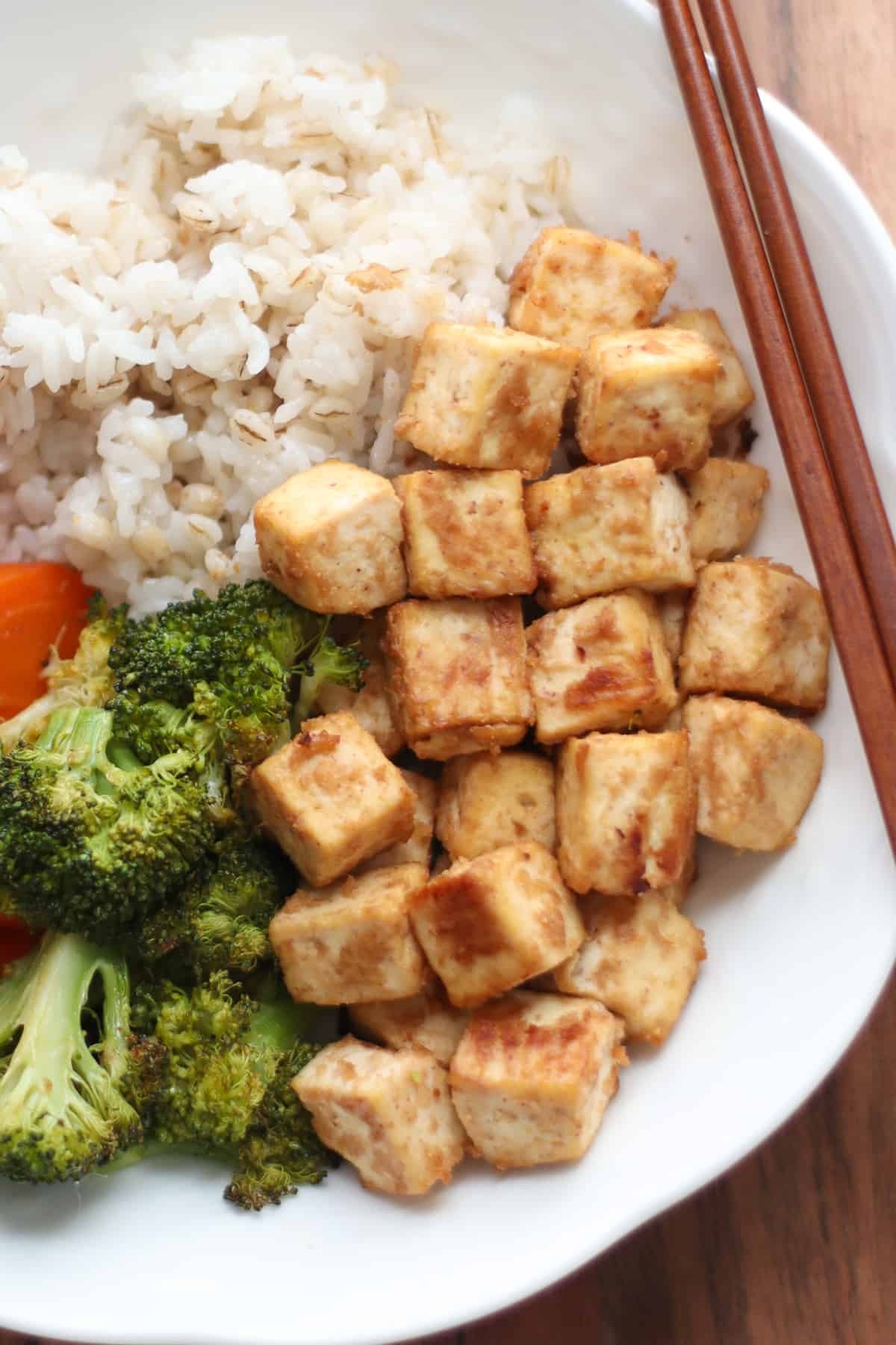 A close up shot of miso tofu in a bowl with rice and vegetables.