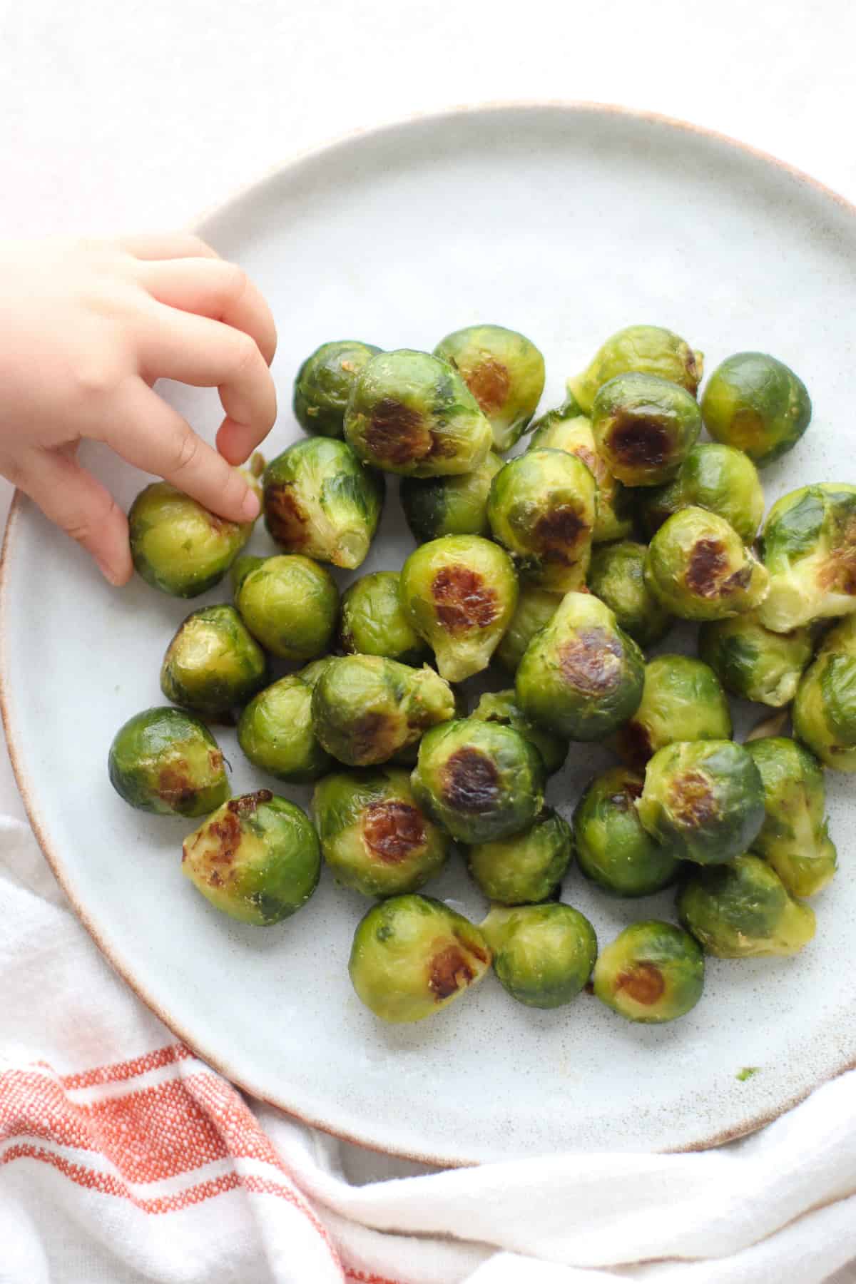 Roasted frozen Brussels sprouts on a plate with a baby's hand grabbing one.