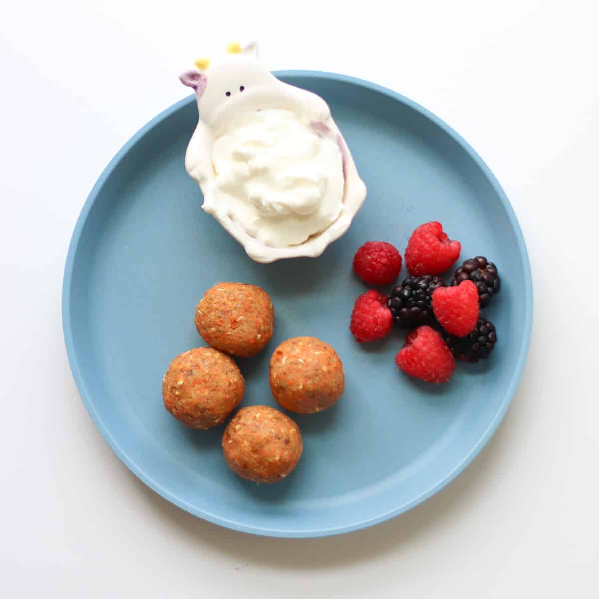 Carrot balls with berries and yogurt on a blue plate.