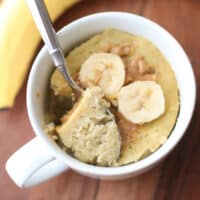 Banana mug cake in a cup with sliced banana and peanut butter drizzle.