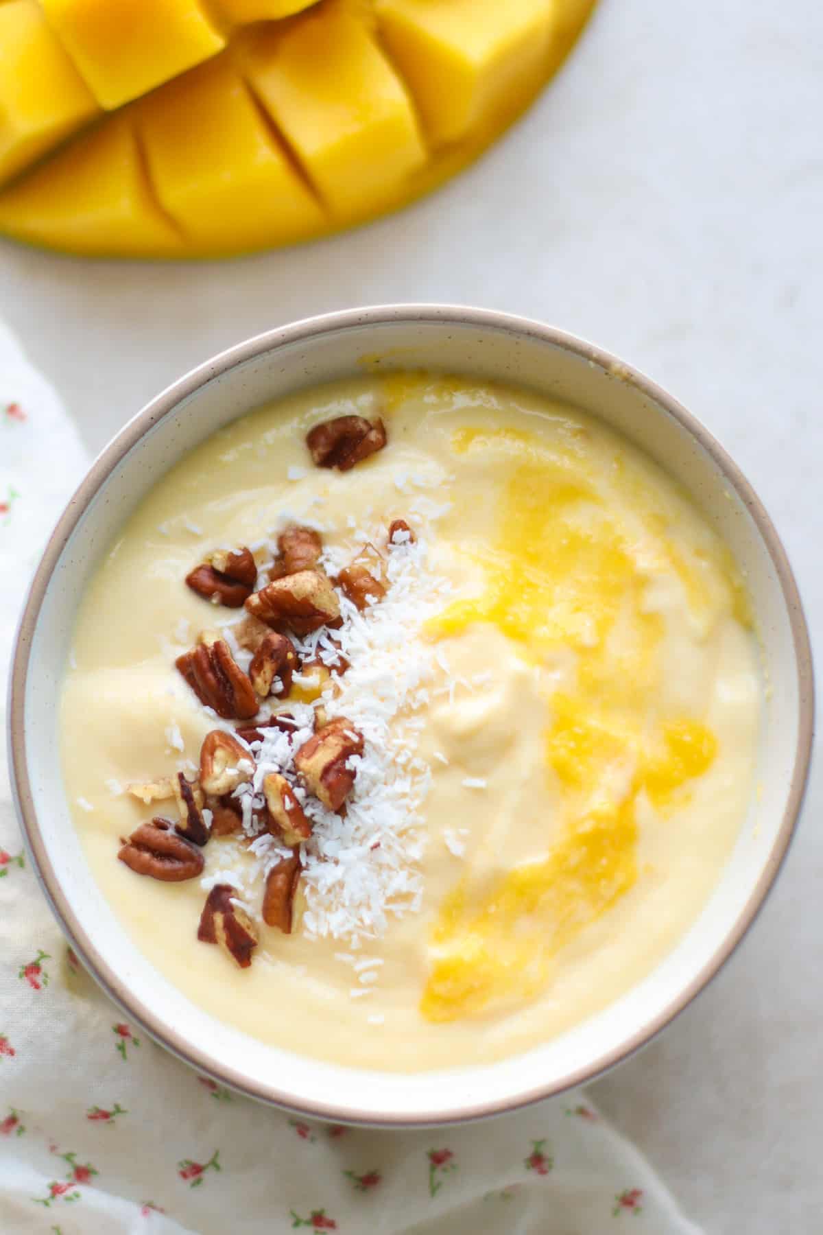 Close up shot of mango yogurt with chopped pecans and coconut flakes.