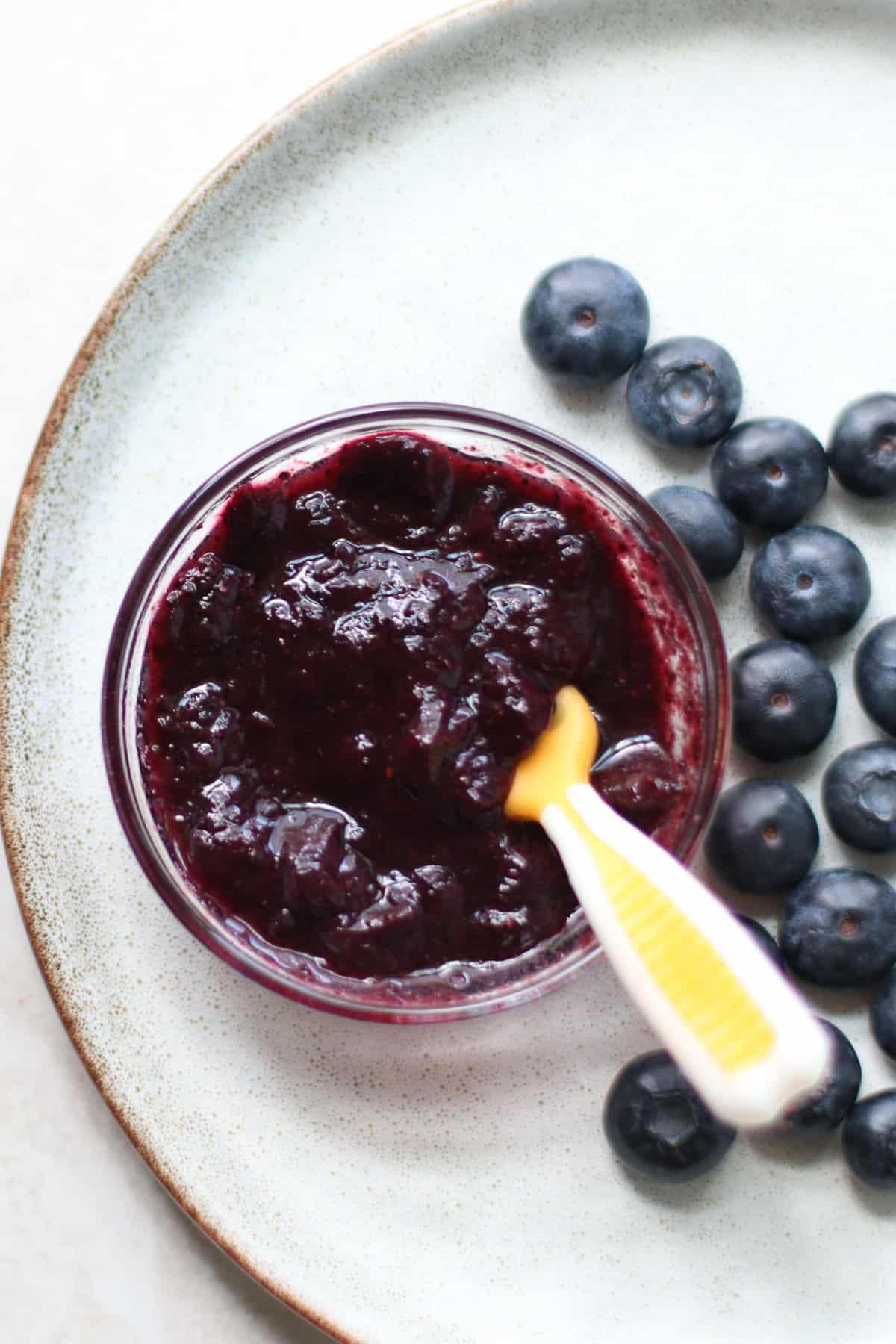 Blueberry puree in a small bowl with a baby spoon.