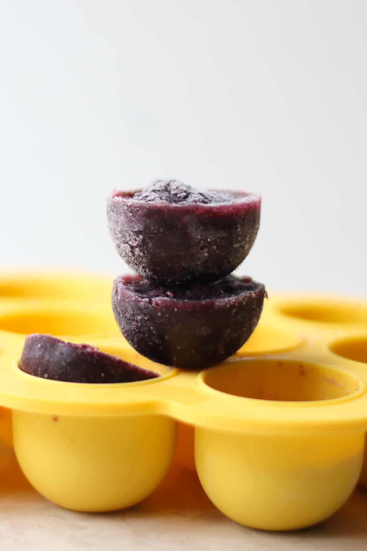 Two stacked frozen blueberry puree cubes placed on a silicone tray.