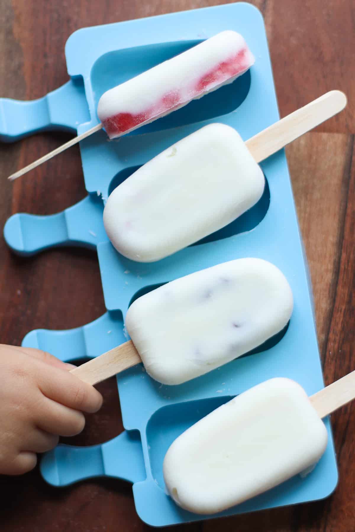 Four frozen yogurt bars placed on top of blue popsicle mold.