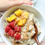 A bowl of steel cut oats with raspberries, mangoes, and peanut butter.