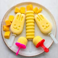 An overhead shot of fun shaped mango popsicles on a plate.