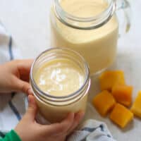 a slightly angled shot of mango shake in two glass jars with toddler holding one.