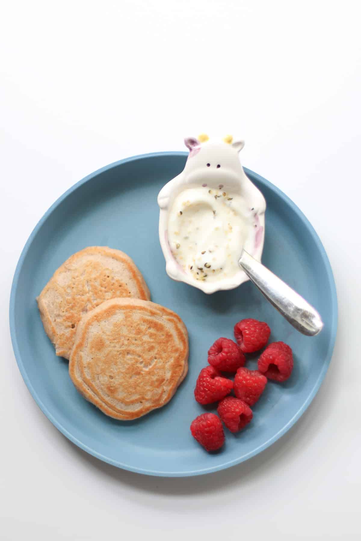 Two pancakes with raspberries and yogurt on a blue plate.