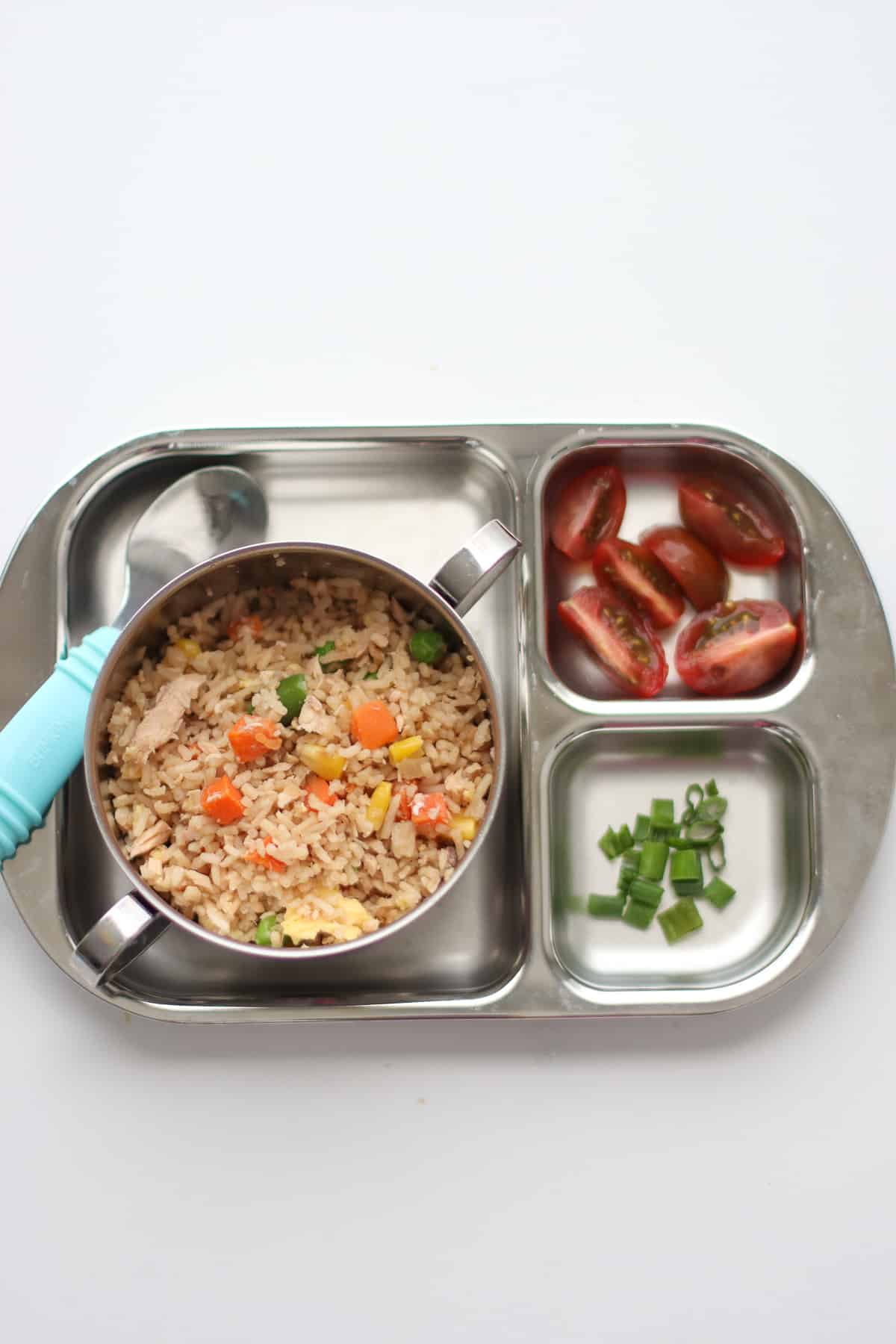 A toddler's stainless steel plate and bowl with rice and a side of quartered cherry tomatoes and chopped green onion.