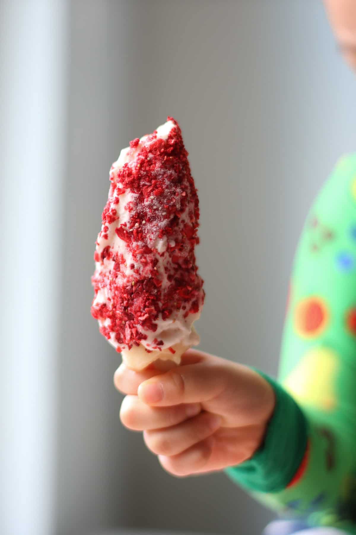 A toddler holding the yogurt covered banana pops rolled in freeze-dried strawberries.