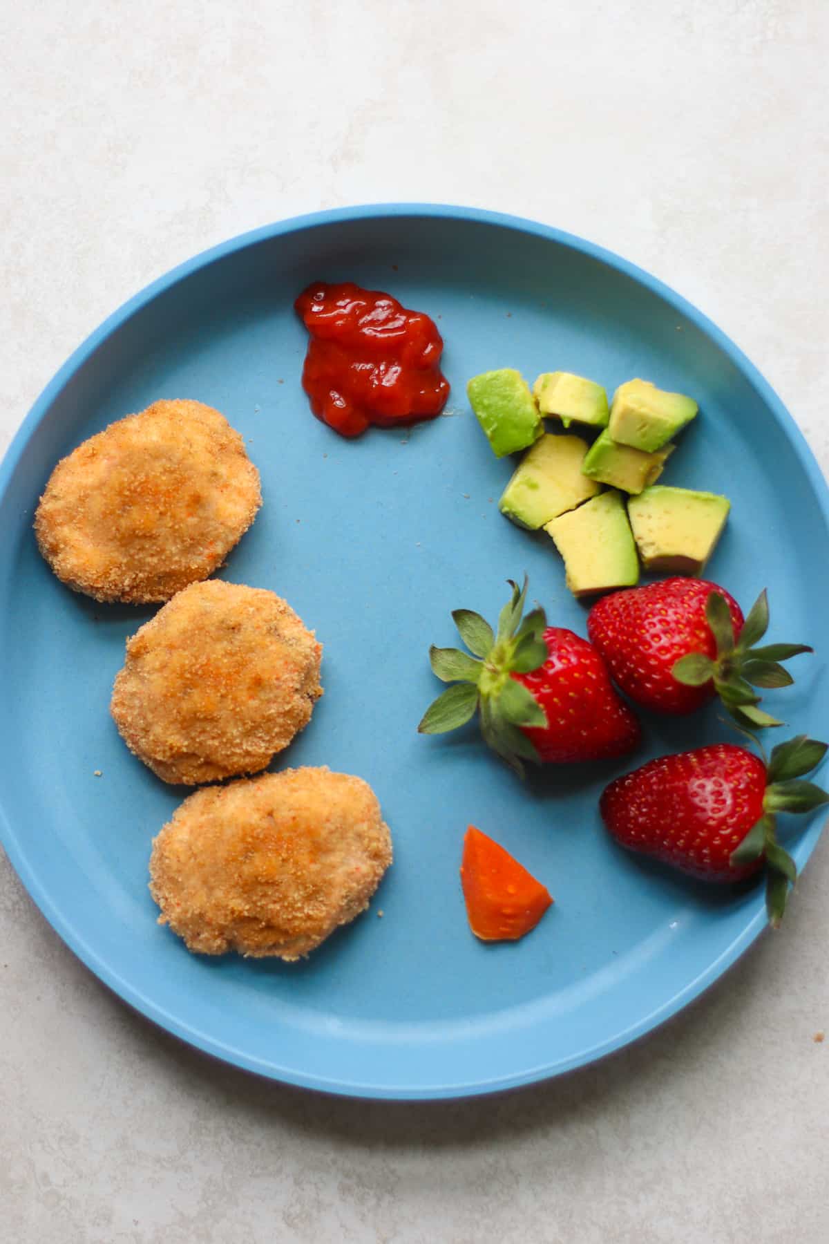 Three nuggets with ketchup, avocado, strawberries, and a tiny piece of carrot.