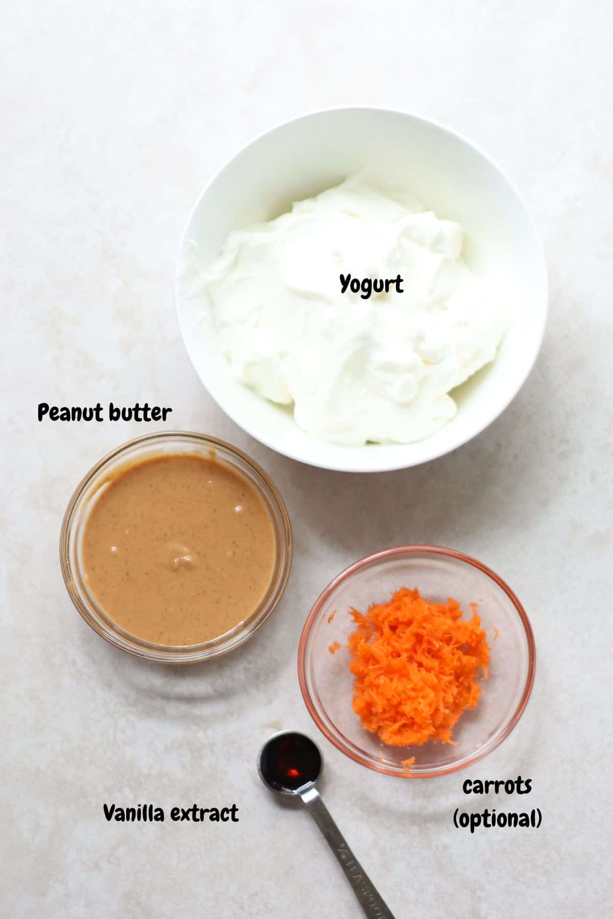 Yogurt, peanut butter, grated carrots, and vanilla extract on a white background.