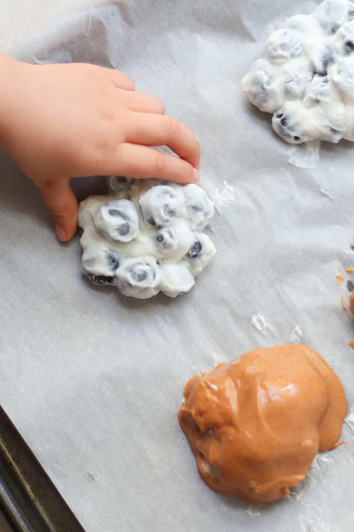 Frozen yogurt covered blueberries with toddler's hand.