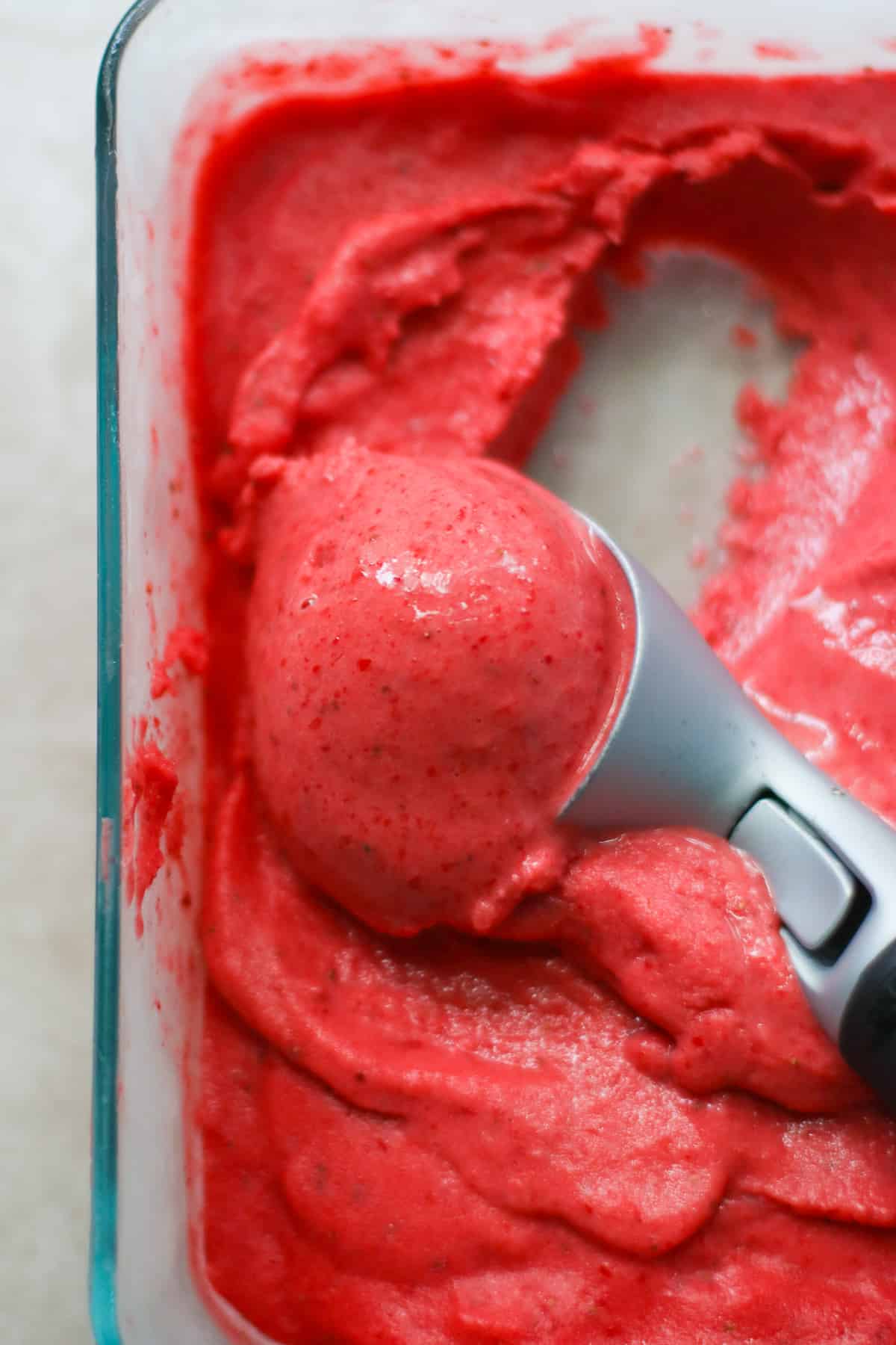 Strawberry sorbet being scooped inside a container.