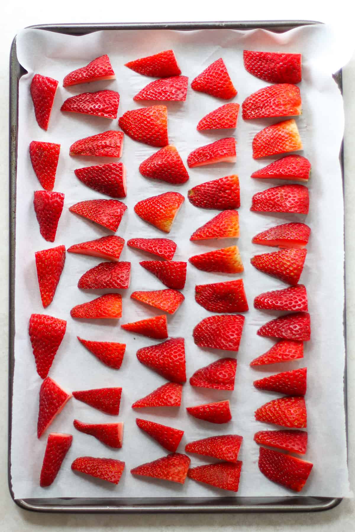 Sliced strawberries laid out on a parchment lined baking sheet.