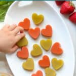 Green and red heart shaped gummies on a white plate.