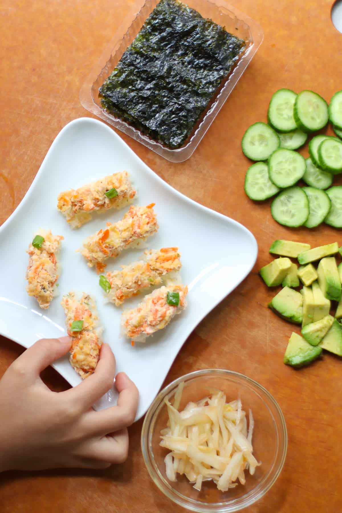 Sushi bake sliced into finger shapes with seaweed sheet, kimchi, cucumber, and avocado on the side.